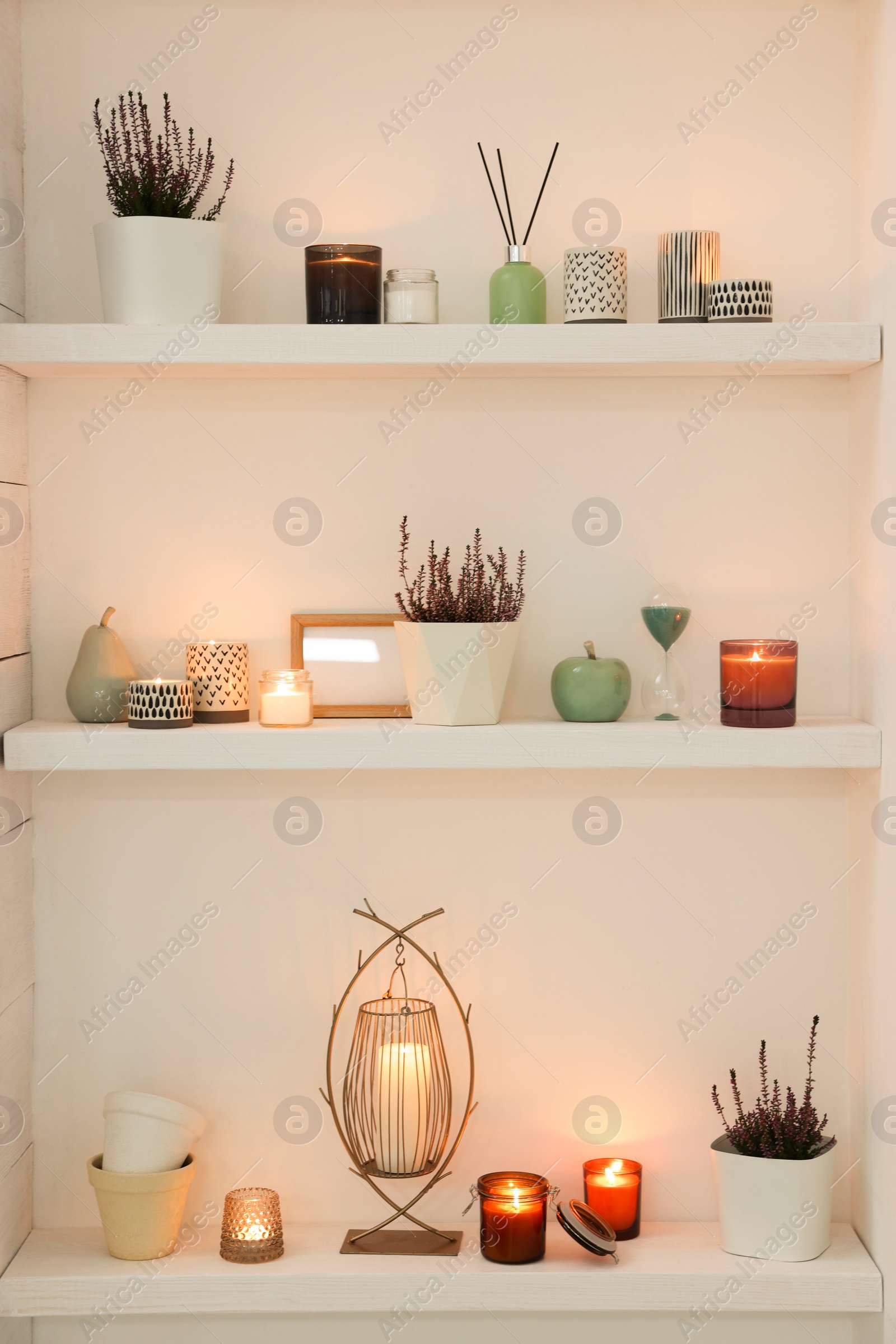 Photo of Burning wax candles and different decor on shelves