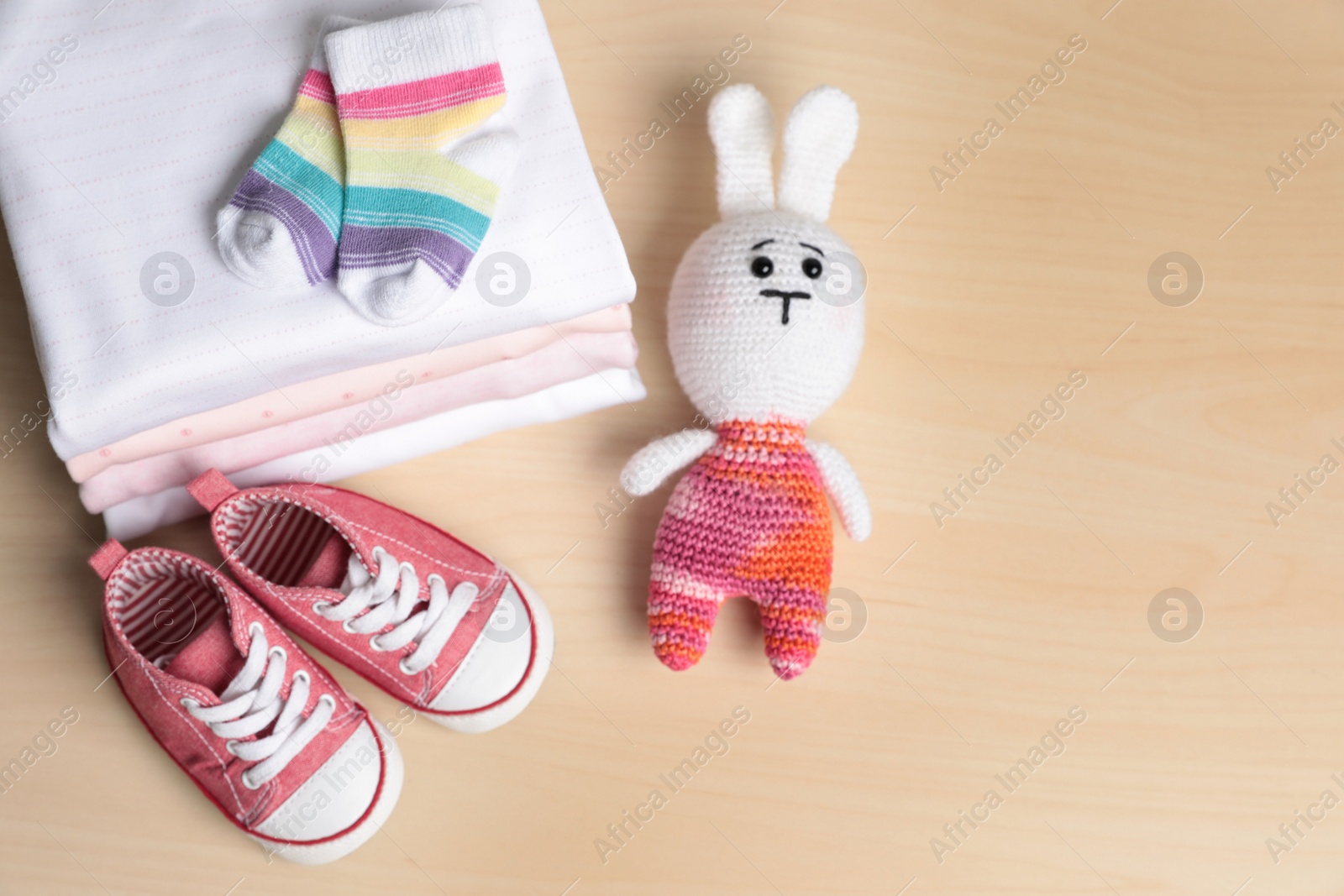 Photo of Baby clothes, shoes and toy on wooden table, flat lay. Space for text