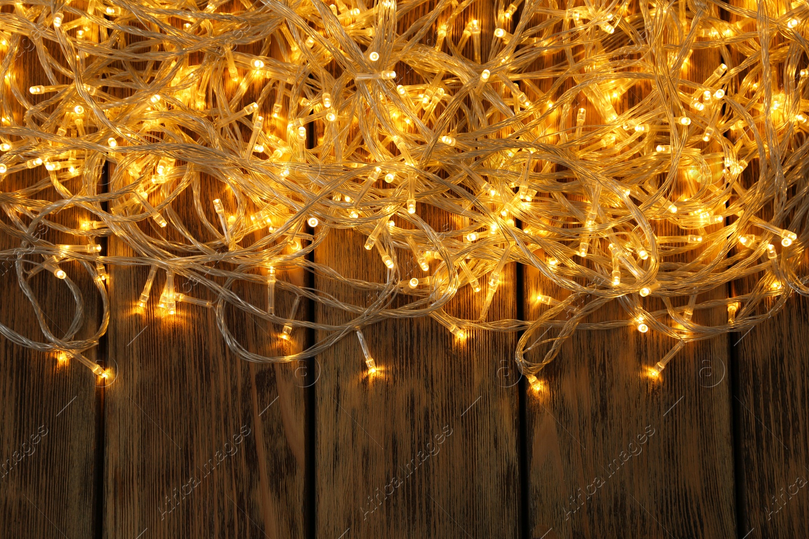 Photo of Glowing Christmas lights on wooden background, top view