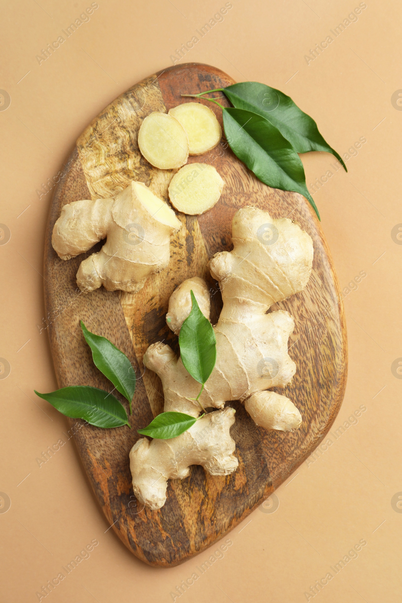 Photo of Fresh ginger with green leaves on light pale brown background, top view