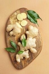 Fresh ginger with green leaves on light pale brown background, top view