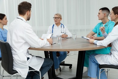 Photo of Medical conference. Team of doctors listening to speaker at wooden table in clinic