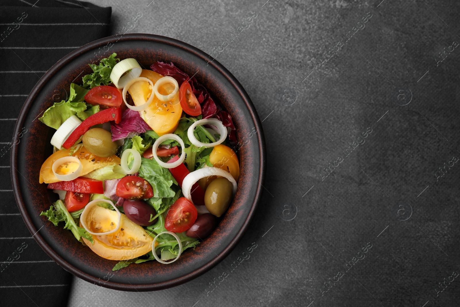 Photo of Bowl of tasty salad with leek and olives on brown table, top view. Space for text