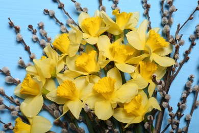 Photo of Bouquet of beautiful yellow daffodils and willow flowers on light blue wooden table, top view