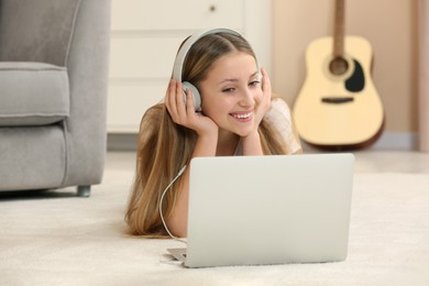 Photo of Teenage girl with headphones using laptop at home