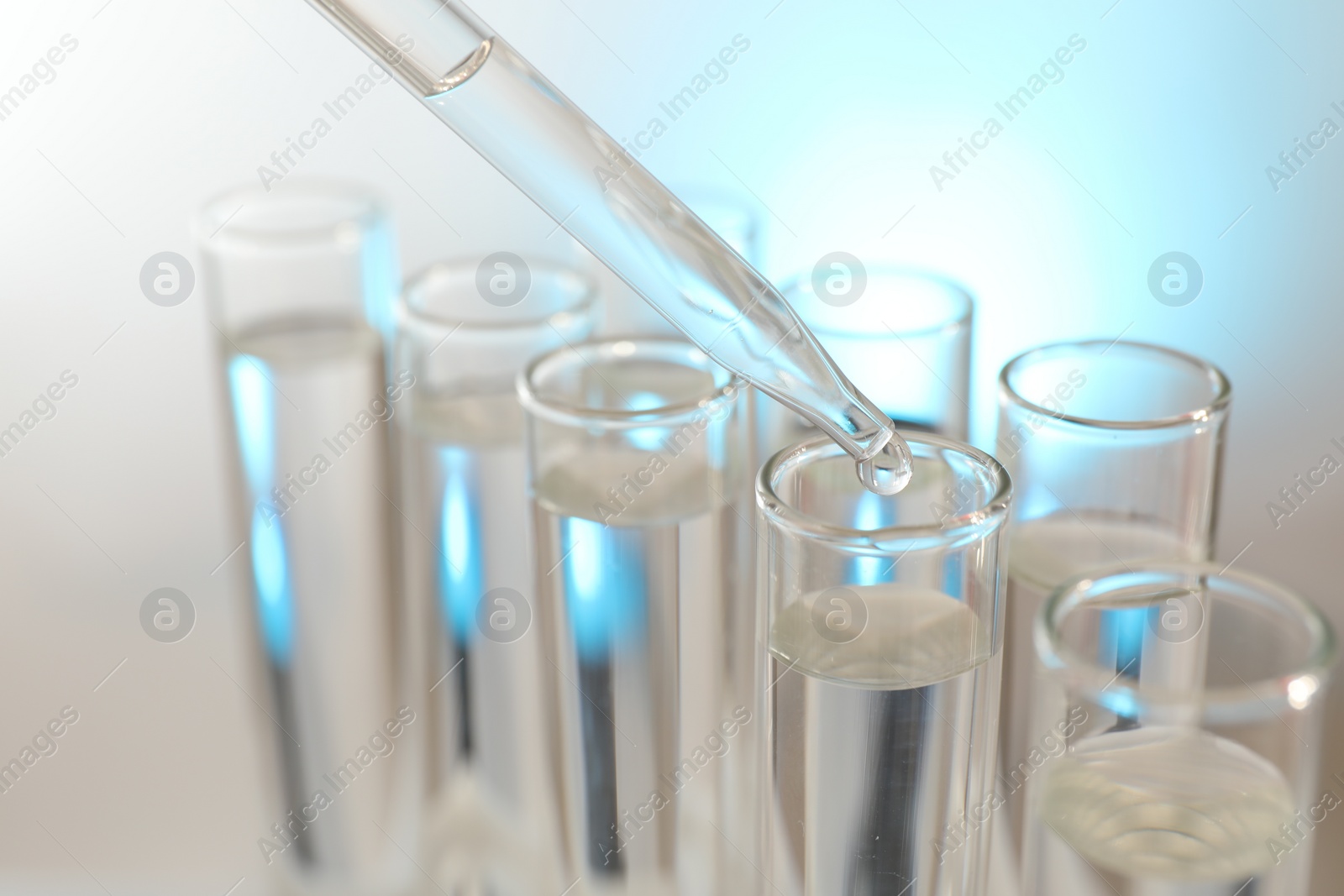 Photo of Dripping liquid from pipette into test tube on light background, closeup