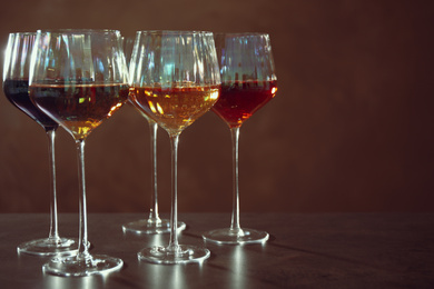 Elegant glasses with different wines on table against brown background