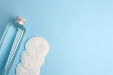 Photo of Bottle of makeup remover and cotton pads on light blue background, flat lay. Space for text