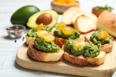 Photo of Tasty bruschettas with avocado and yellow cherry tomatoes on white wooden table, closeup