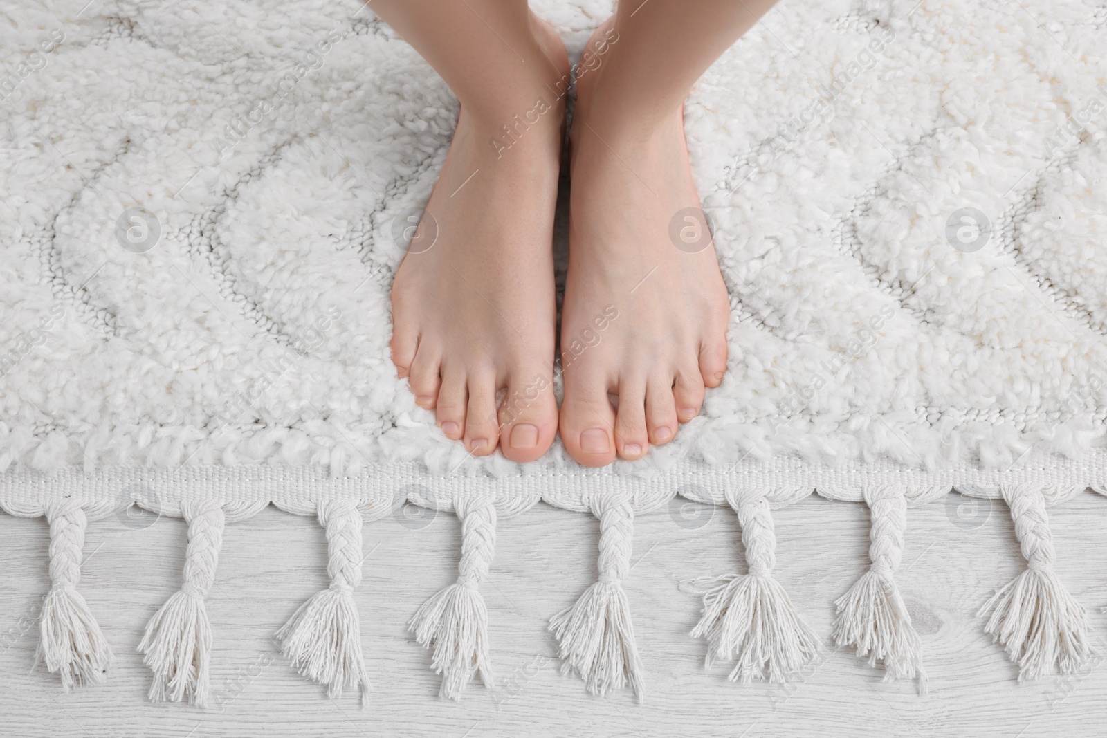 Photo of Woman standing on soft white carpet at home, top view