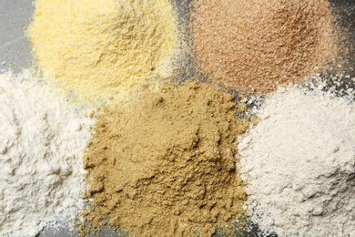 Piles of different flour types on grey table, top view