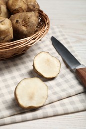 Photo of Wicker basket and many Jerusalem artichokes with knife on white wooden table