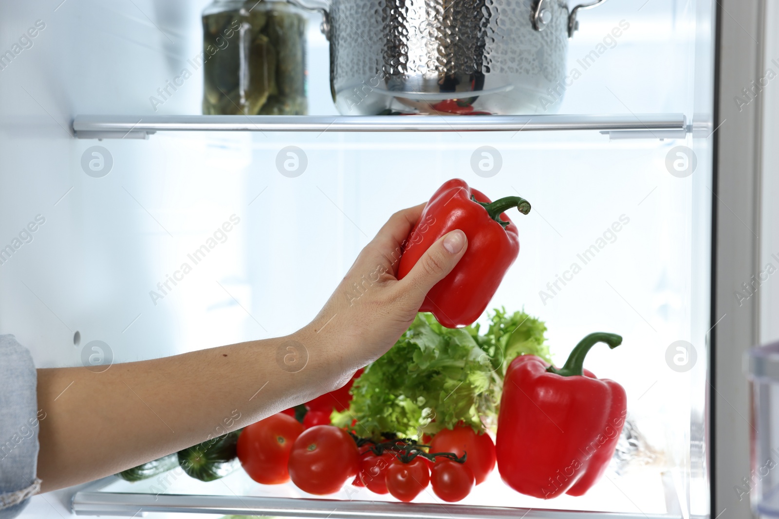 Photo of Young woman taking red bell pepper out of refrigerator, closeup