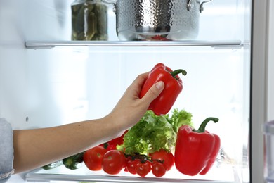 Photo of Young woman taking red bell pepper out of refrigerator, closeup