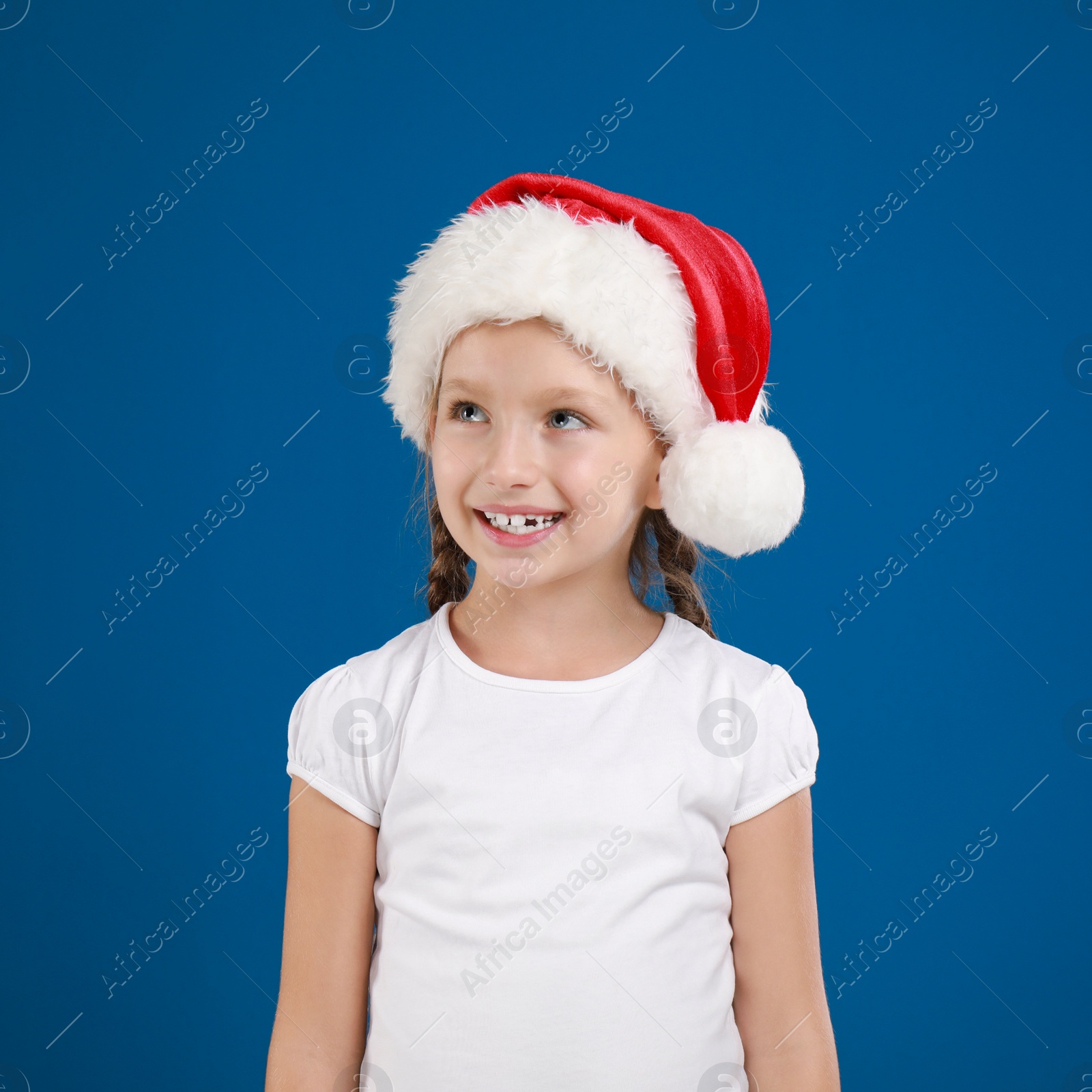 Image of Happy little child in Santa hat on blue background. Christmas celebration