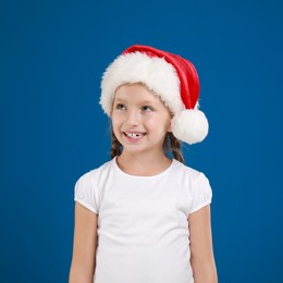 Happy little child in Santa hat on blue background. Christmas celebration