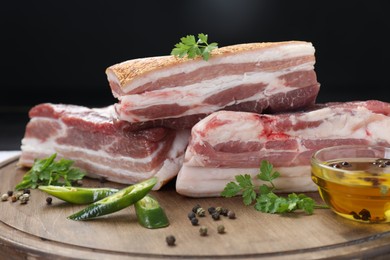 Photo of Pieces of raw pork belly, chili pepper, peppercorns, oil and parsley on wooden board, closeup