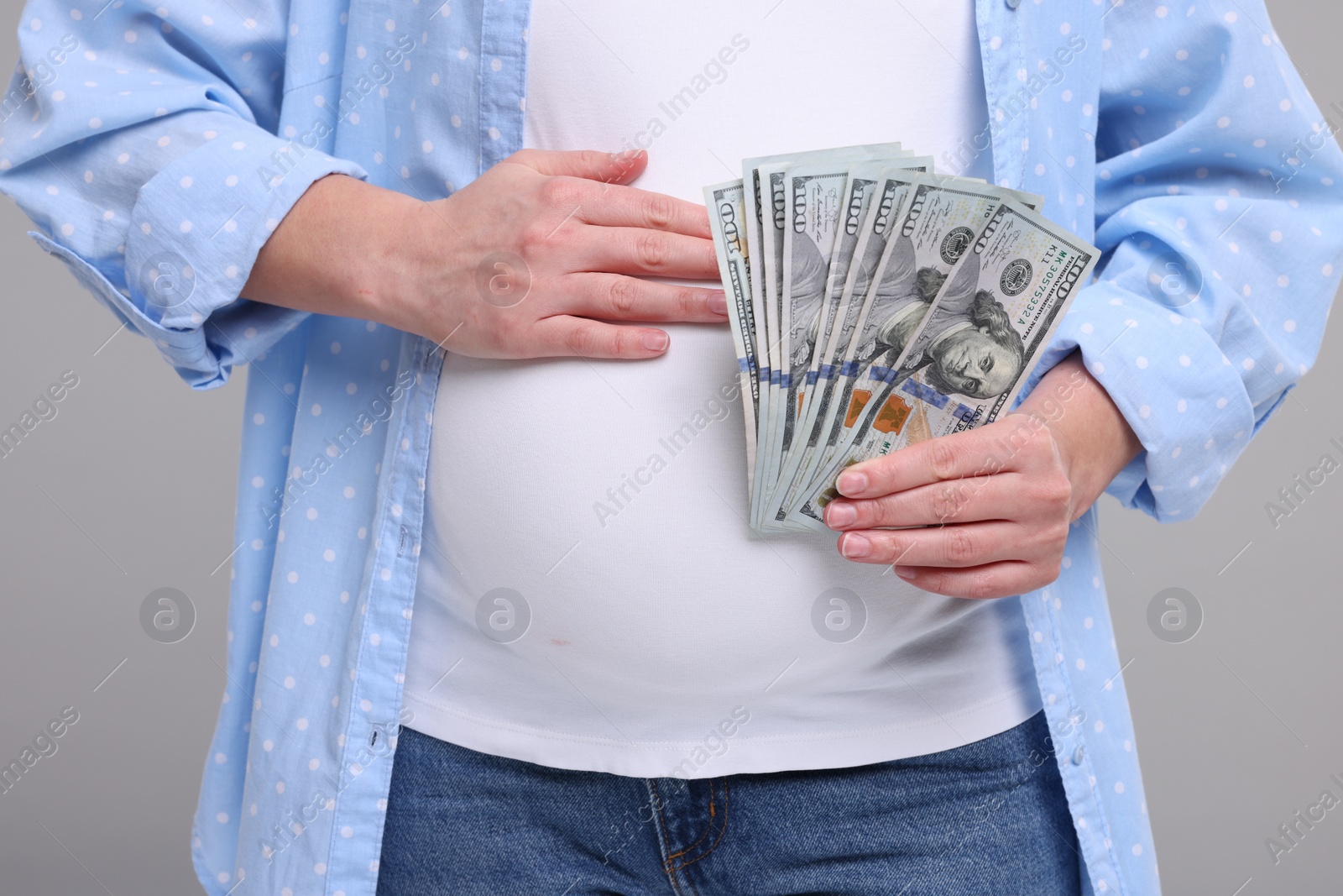 Photo of Surrogate mother. Pregnant woman with dollar banknotes on light grey background, closeup