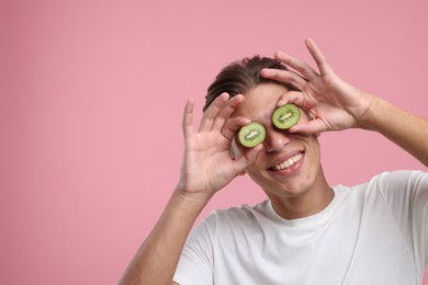 Smiling man covering eyes with halves of kiwi on pink background. Space for text
