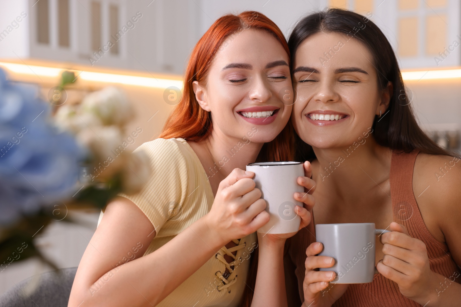 Photo of Portrait of happy young friends with cups of drink at home