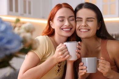 Photo of Portrait of happy young friends with cups of drink at home