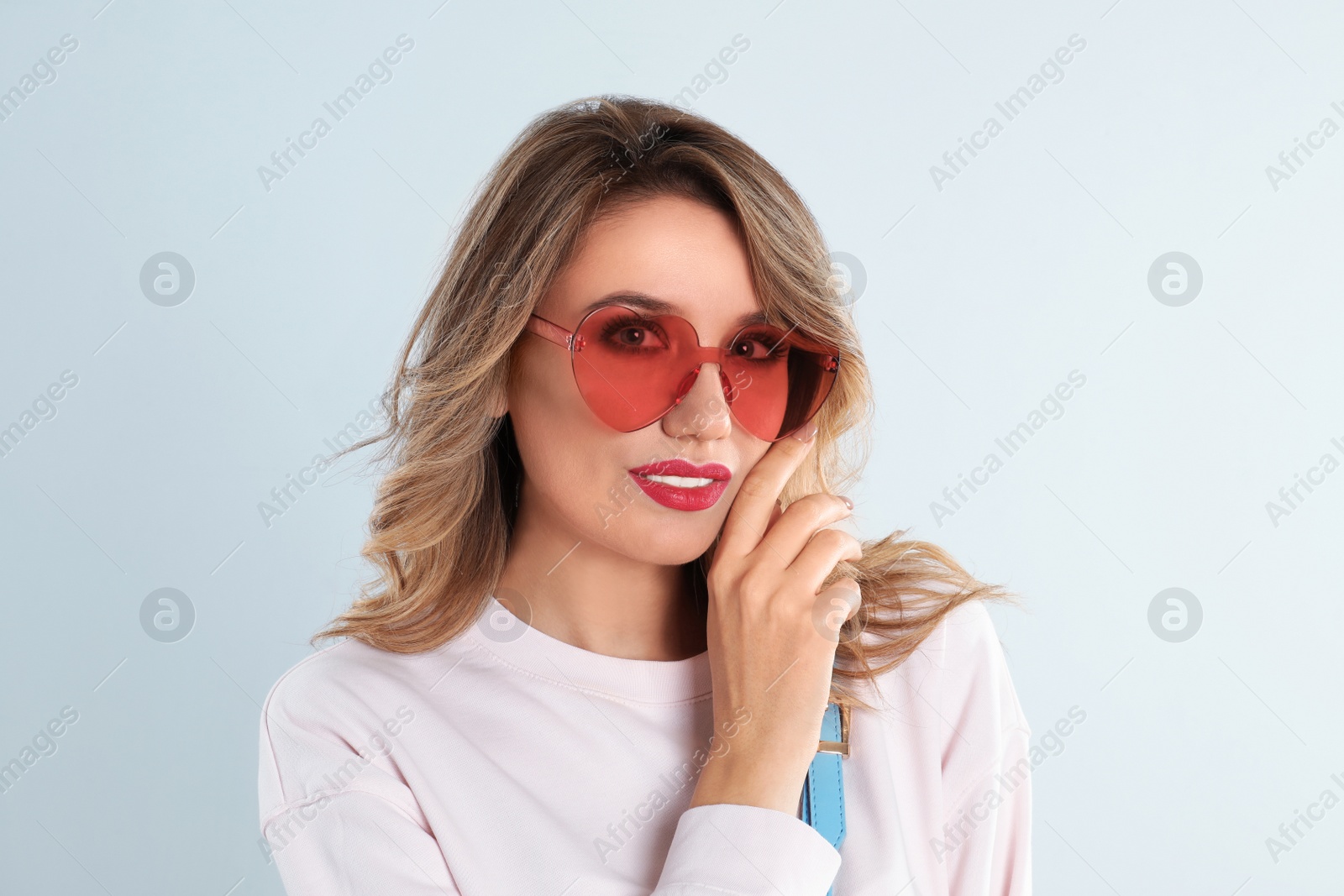 Photo of Young woman wearing heart shaped sunglasses on light grey background