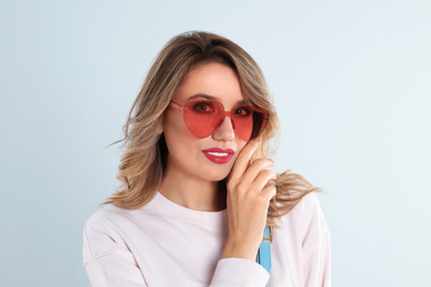 Young woman wearing heart shaped sunglasses on light grey background