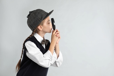 Photo of Cute little detective with magnifying glass on grey background. Space for text
