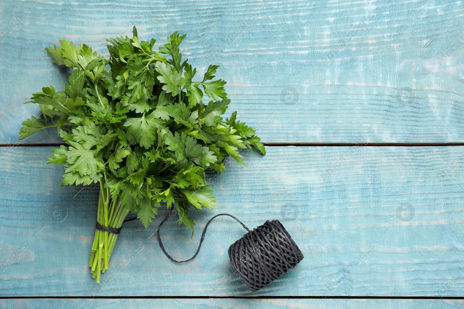 Photo of Bunch of fresh green parsley and rope on blue wooden table, flat lay. Space for text