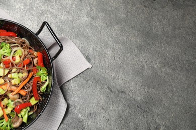 Stir fried noodles with mushrooms and vegetables in wok on grey table, top view. Space for text