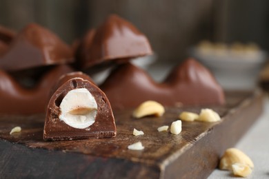 Photo of Tasty chocolate bar with nuts on wooden board, closeup. Space for text