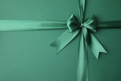 Photo of Bright satin ribbon with bow on green background, top view