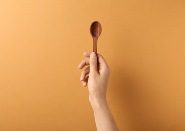 Woman holding empty wooden spoon on color background, closeup. Space for text