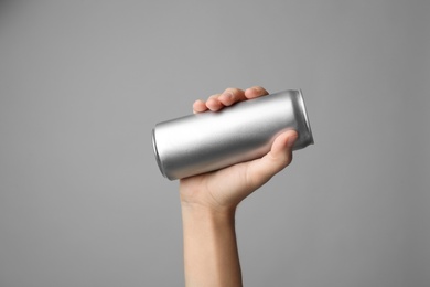 Woman holding aluminum can with beverage on grey background, closeup. Space for design