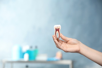 Dentist holding educational model of tooth on blurred background. Space for text