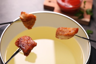 Oil in fondue pot and forks with fried meat pieces on table, closeup