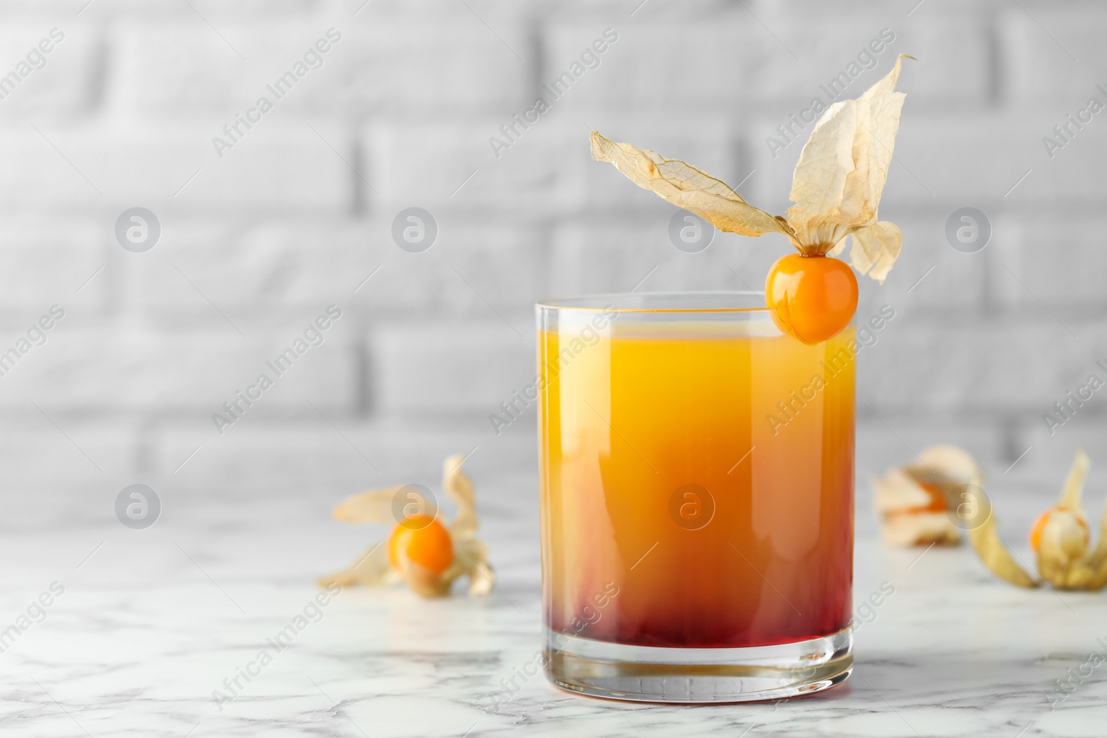 Photo of Delicious cocktail decorated with physalis fruit on white marble table. Space for text