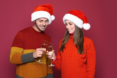 Young couple in Santa hats clinking glasses of champagne on color background. Christmas celebration