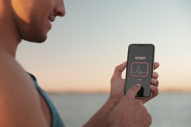Man using fitness app on smartphone near river at sunset, closeup