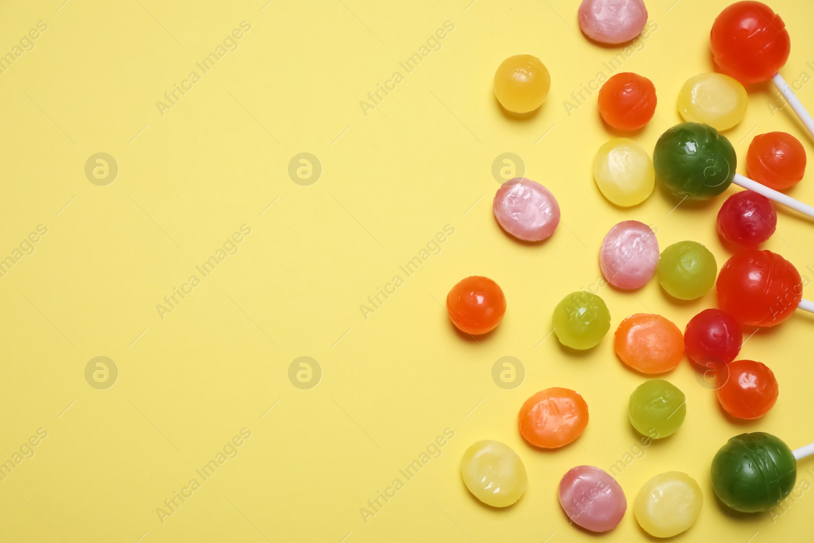 Photo of Many different hard candies on yellow background, flat lay. Space for text