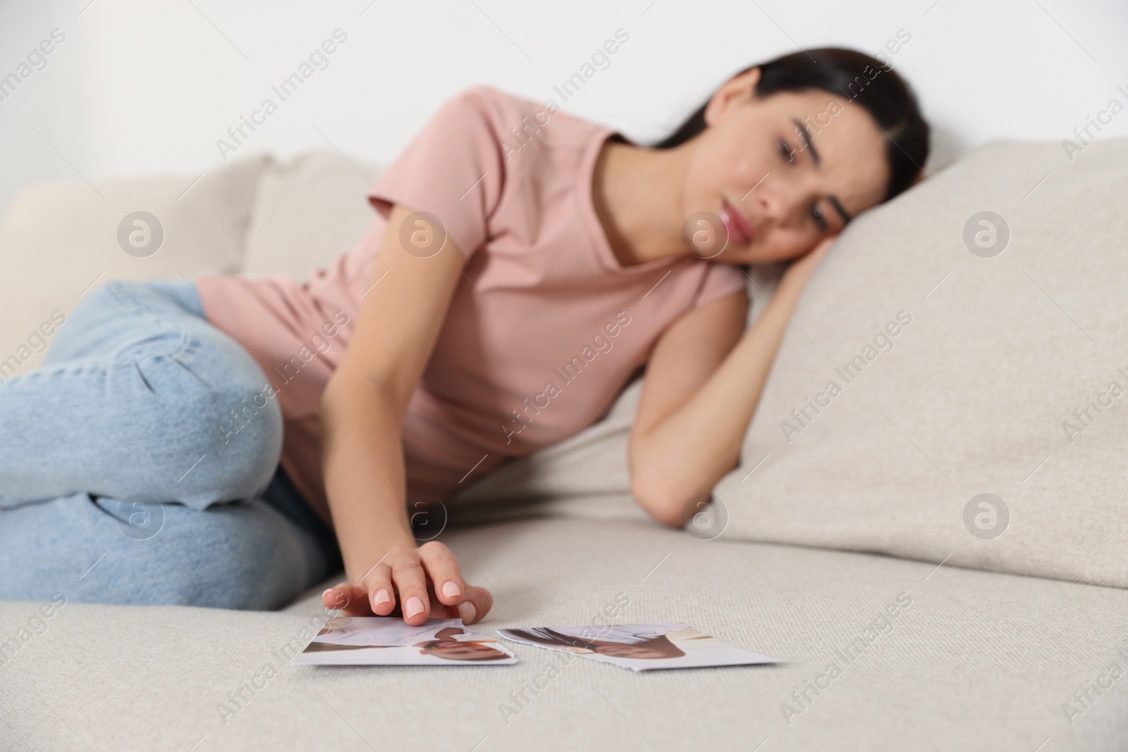 Photo of Upset woman looking at parts of torn photo indoors, selective focus. Divorce concept