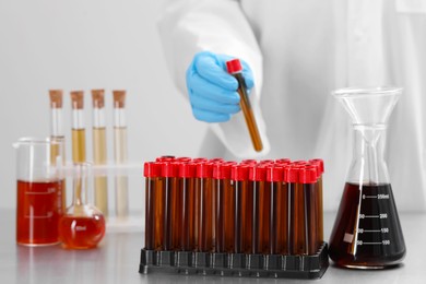 Photo of Scientist holding test tube with brown liquid near different laboratory glassware on table, selective focus