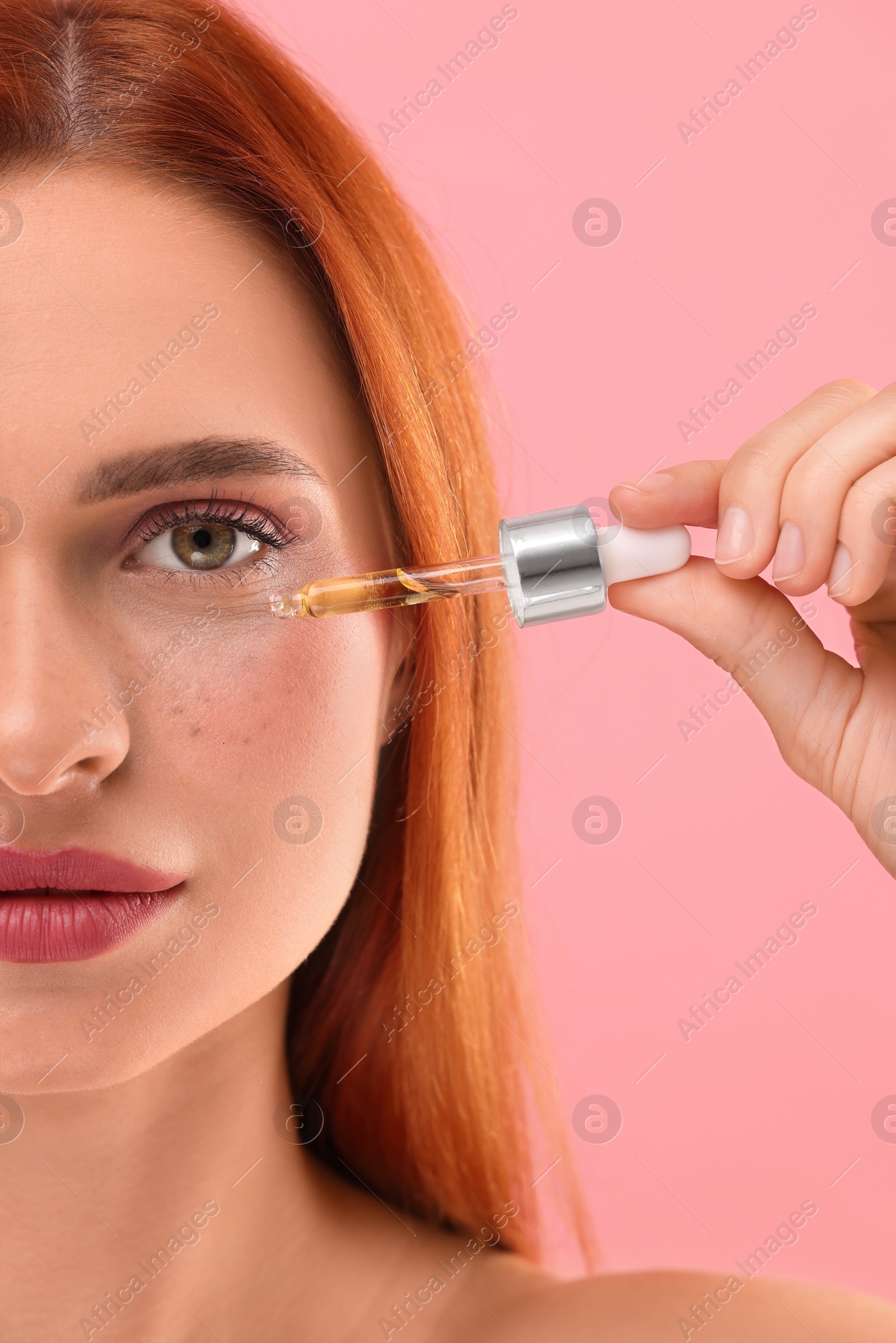 Photo of Beautiful young woman applying cosmetic serum onto her face on pink background, closeup