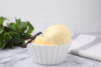 Photo of Delicious ice cream and vanilla pods on white marble table, closeup