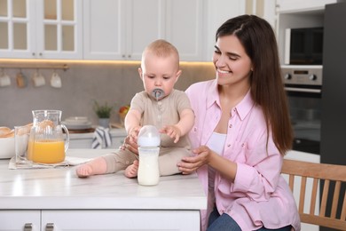Photo of Mother and her cute little baby with feeding bottle of milk in kitchen, space for text