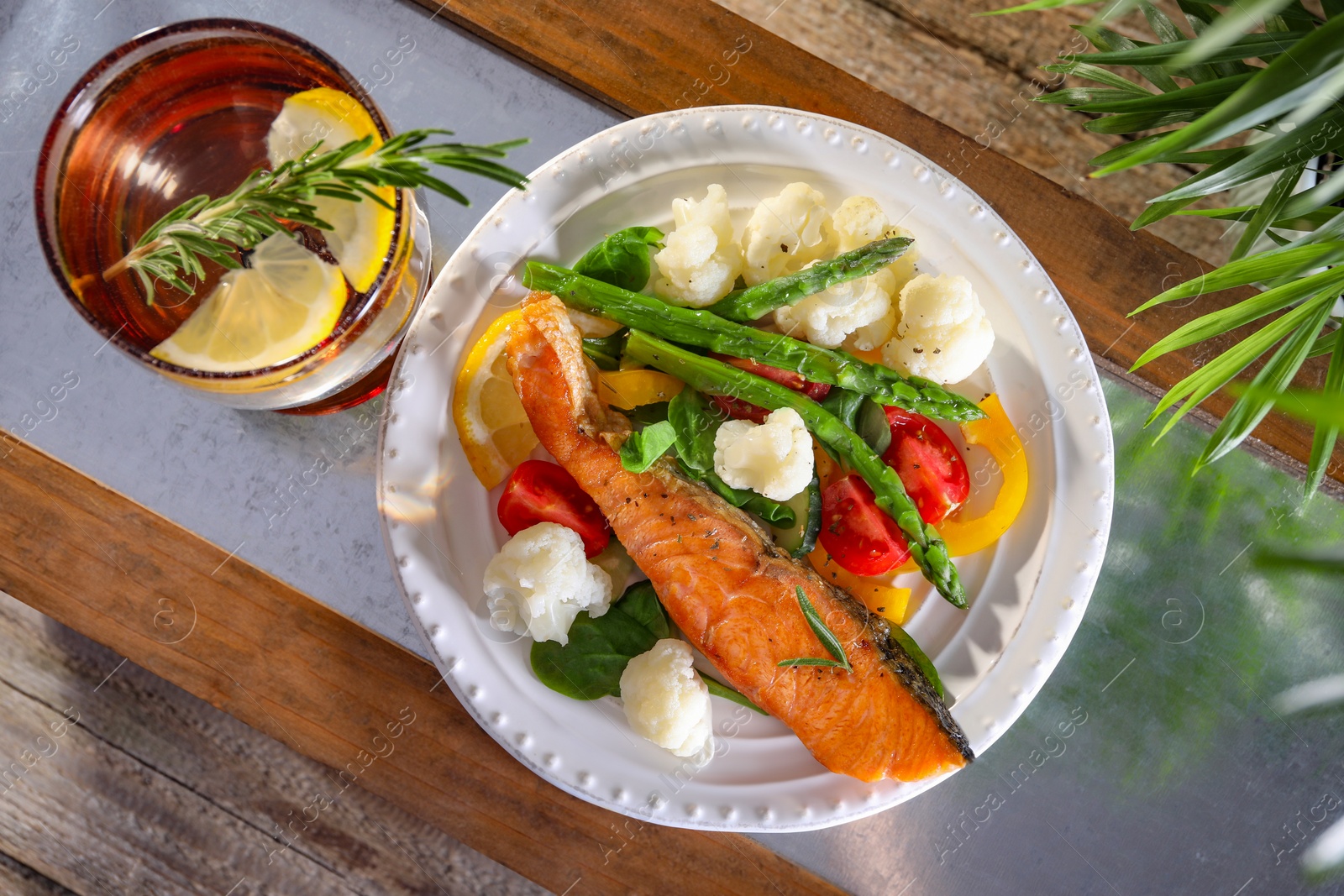 Photo of Healthy meal. Piece of tasty grilled salmon with vegetables and glass of refreshing drink on wooden table, top view