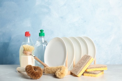 Photo of Cleaning supplies for dish washing and plates on grey table against light blue background