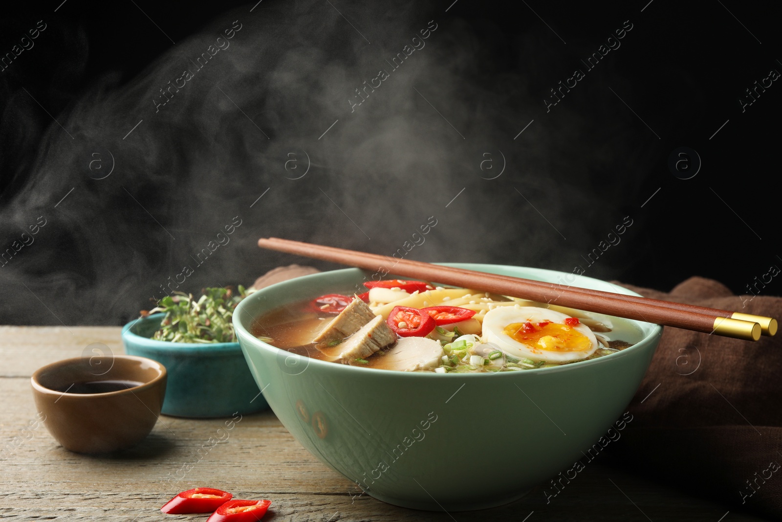 Photo of Delicious ramen in bowl on wooden table against black background, closeup. Noodle soup