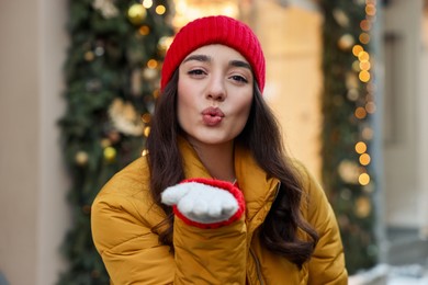 Portrait of beautiful woman blowing kiss on city street in winter