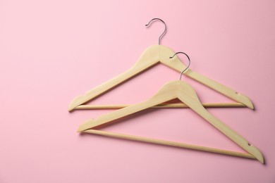 Wooden hangers on pink background, top view. Space for text